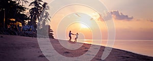 Beautiful young couple in love whirls holding hands on the beach at sunset during the honeymoon vacation travel