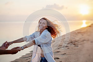 Beautiful young couple in love whirls holding hands on the beach at sunset during the honeymoon vacation travel