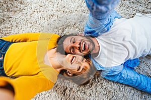 Beautiful young couple of lovers lying on the carpet at home smiling at the camera