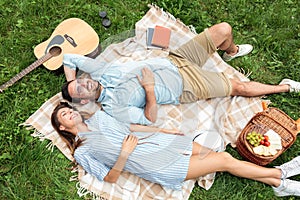 Beautiful young couple lying next to each-other and relaxing on a picnic blanket, enjoying their day away from urban life