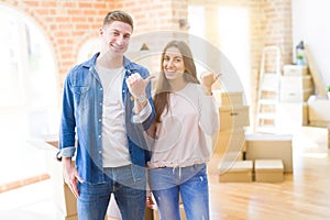 Beautiful young couple moving to a new house smiling with happy face looking and pointing to the side with thumb up