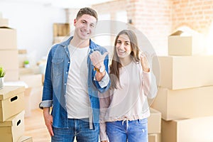 Beautiful young couple moving to a new house smiling with happy face looking and pointing to the side with thumb up