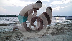 Beautiful young couple is painting on the sand by the river.