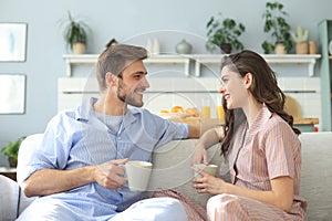 Beautiful young couple in pajamas is looking at each other and smiling on a sofa in the living room