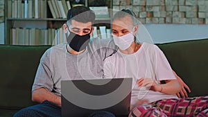 Beautiful young couple in the pandemic of Coronavirus chatting on the laptop using a webcam wearing protective mask they