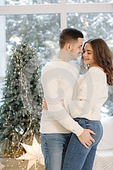 Beautiful young couple posing to photographer at New Year studio. Christmas tree. Snow outside