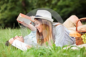 Beautiful young couple relaxing in city park, reading books while lying on a picnic blanket