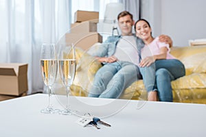 beautiful young couple relaxing on couch while moving into new home with champagne glasses and keys