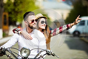 Beautiful young couple riding scooter together while happy woman pointing away and smiling