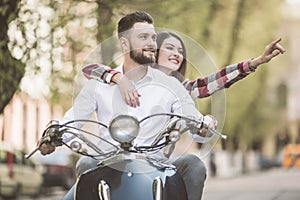 Beautiful young couple riding scooter together while happy woman pointing away and smiling. toned