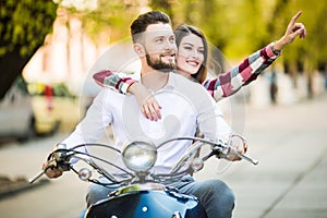 Beautiful young couple riding scooter together while happy woman pointing away and smiling