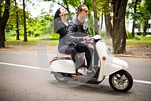 Beautiful young couple riding scooter together, woman hugging her boyfriend. Side view on speed.