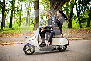 Beautiful young couple riding scooter together, woman hugging her boyfriend. Side view on speed.