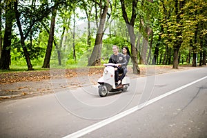 Beautiful young couple riding scooter together, woman hugging her boyfriend. Side view on speed.