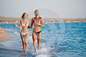 Beautiful young couple runnung at sea water edge and holding hands