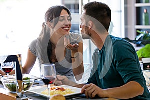 Beautiful young couple sharing single spaghetti getting closer to kissing in the kitchen at home