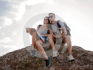 Beautiful young couple sitting on the rock and looking at the map