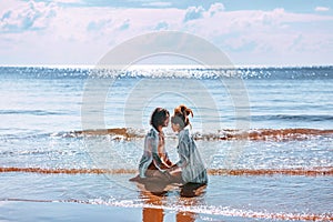 Beautiful young couple sitting on sand in front of each other in sea waves. Young man and woman love story on the beach
