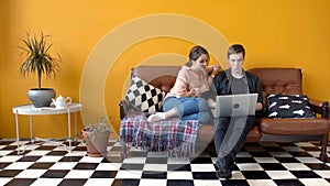 Beautiful young couple sitting together at laptop on couch. Stock footage. Couple of students together watching