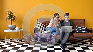 Beautiful young couple sitting together at laptop on couch. Stock footage. Couple of students together watching