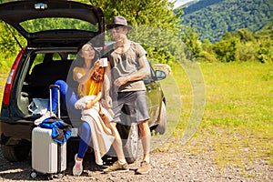 Beautiful young couple sitting in the trunk of a car and admire the beautiful scenery on the mountain.