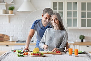 Beautiful young couple smiling while preparing vegetable salad in the kitchen at home