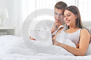 Beautiful young couple on soft bed in morning with laptop