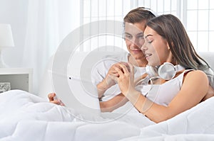 Beautiful young couple on soft bed in morning with laptop