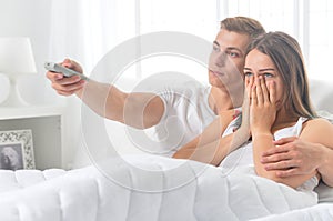 Beautiful young couple on soft bed in morning watching tv