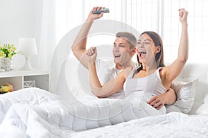 Beautiful young couple on soft bed in morning watching tv