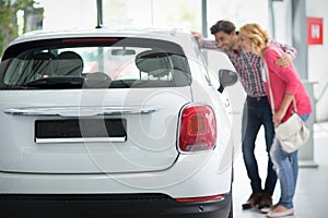 Beautiful young couple standing at the car dealership and making