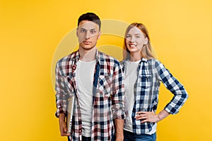 Beautiful young couple of students, man and woman with laptop on yellow background