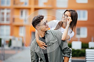 Beautiful young couple in sun glasses looking at each other and smiling while standing outdoors. Girl piggyback