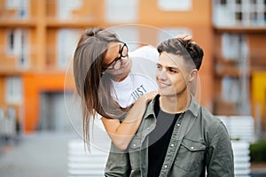 Beautiful young couple in sun glasses looking at each other and smiling while standing outdoors. Girl piggyback