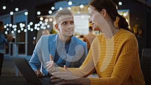Beautiful Young Couple is Using a Laptop while Sitting at a Table in an Outdoors Street Food Cafe.
