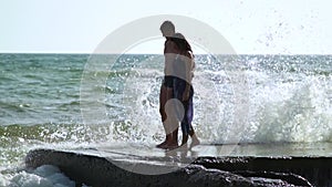 Beautiful young couple walking near the sea in a storm. The waves break about the pier. A guy in swimming trunks, a girl in a swim