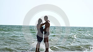 Beautiful young couple walking near the sea in a storm. The waves break about the pier. A guy in swimming trunks, a girl in a swim