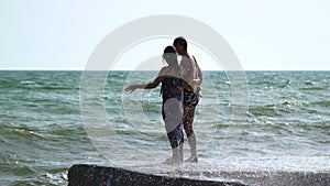 Beautiful young couple walking near the sea in a storm. The waves break about the pier. A guy in swimming trunks, a girl in a swim