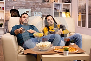 Beautiful young couple watching TV and eating fast food takeaway