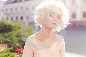 Beautiful young curly blond girl outdoors in the sun at sunset on a bright day