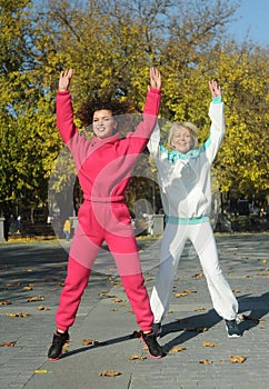 Beautiful young curly hair woman in pink sportswear and middle age 50s woman doing sports outdoors.