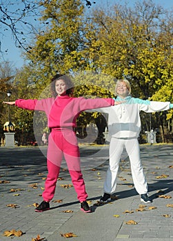 Beautiful young curly hair woman in pink sportswear and middle age 50s woman doing sports outdoors.