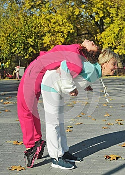 Beautiful young curly hair woman in pink sportswear and middle age 50s woman doing sports outdoors.