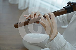 Beautiful young curly woman playing a wooden flute at home near the window