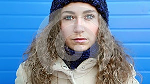 Beautiful young curly woman sad, with blue eyes leaning against blue wall