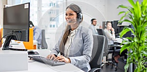 Beautiful young customer service representative wearing headset working on computer at cal center office