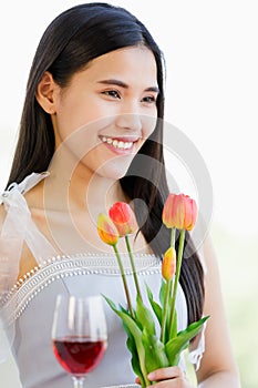 A beautiful young cute black long hair Asian woman holding red wine glass and tulip bunch