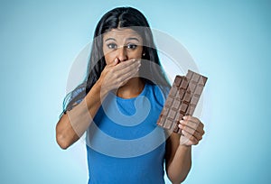 Beautiful young cute and happy latin woman in casual clothes holding big delicious chocolate tablet looking with temptation