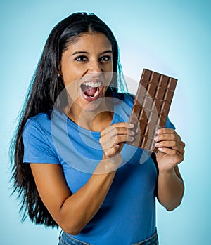 Beautiful young cute and happy latin woman in casual clothes holding big delicious chocolate tablet looking with temptation