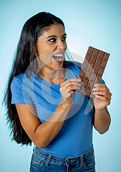 Beautiful young cute and happy latin woman in casual clothes holding big delicious chocolate tablet looking with temptation